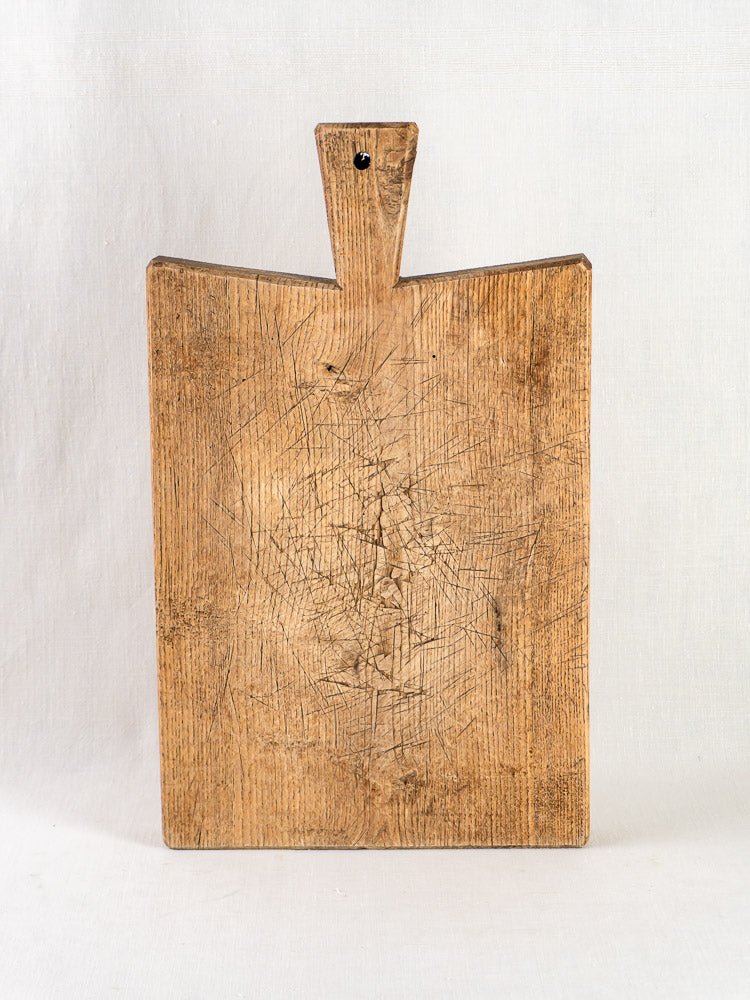 Antique French oak chopping board with handle and knife marks, upright on white background.