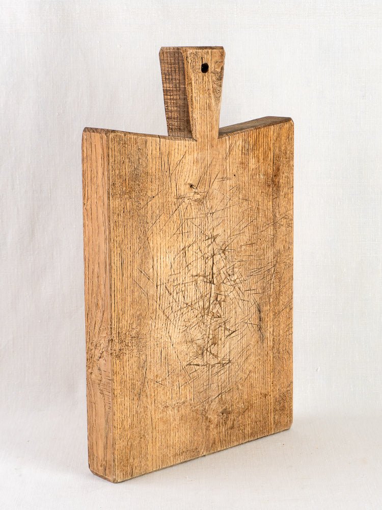 Late 19th-century antique French oak chopping board with knife marks and handle, on light background.