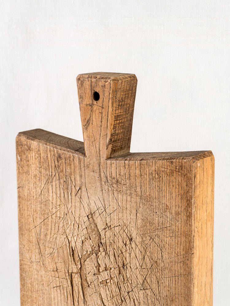 Antique French oak chopping board with rustic handle, visible scratches, and rich wood grain.