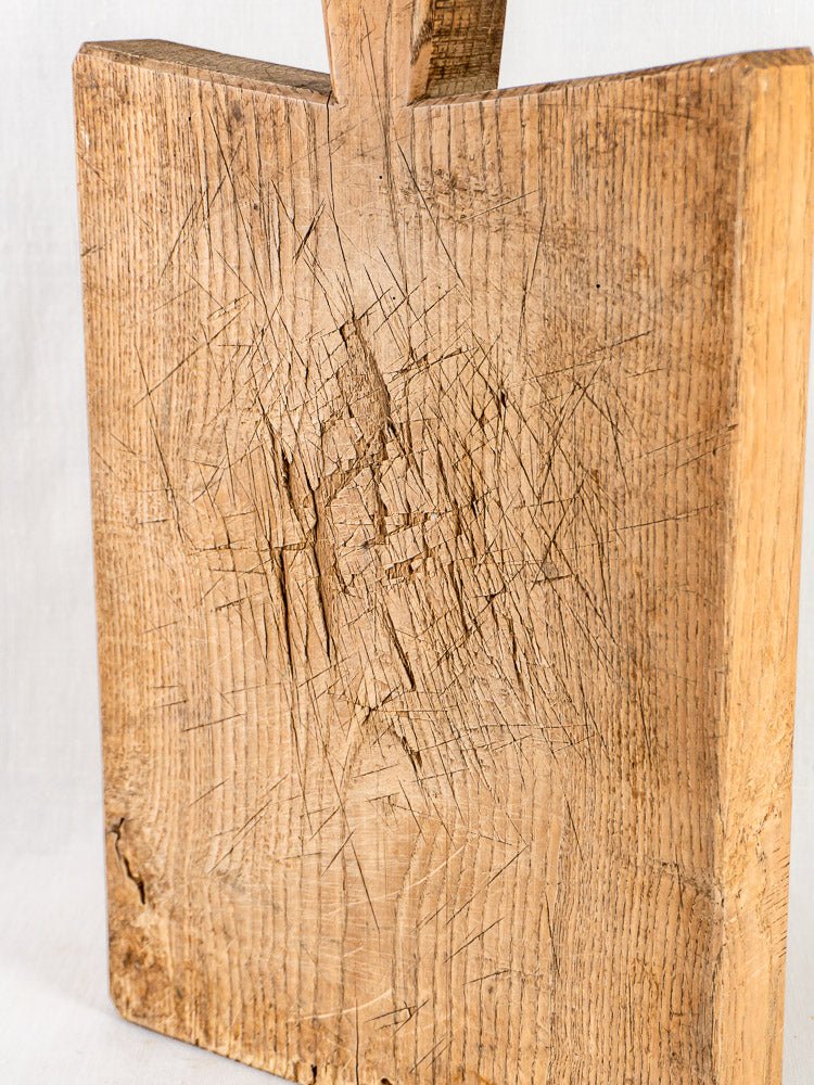 Antique French oak chopping board, late 19th century, with deep knife marks and sturdy handle upright.