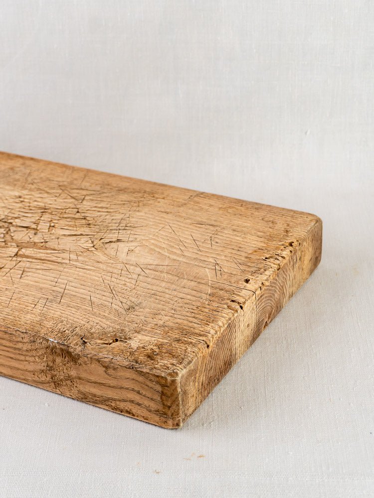 Antique French oak chopping board with rectangular form, knife marks, and worn edges on light fabric.