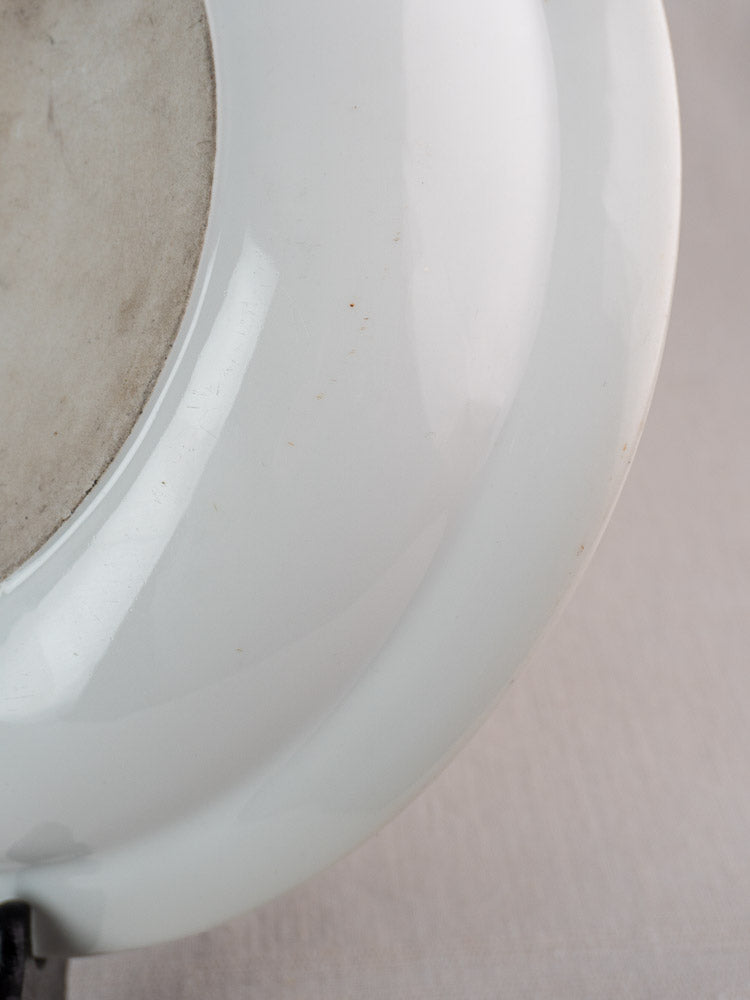 Glossy white French Aluminite bowl by Frugier Limoges, rounded edge, matte unglazed base, neutral fabric background.