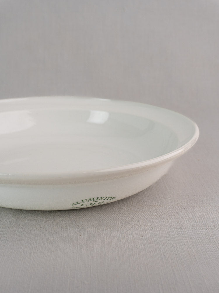 Antique French Aluminite bowl by Frugier Limoges, white ceramic with green "ALUMINIA" mark on light gray surface.
