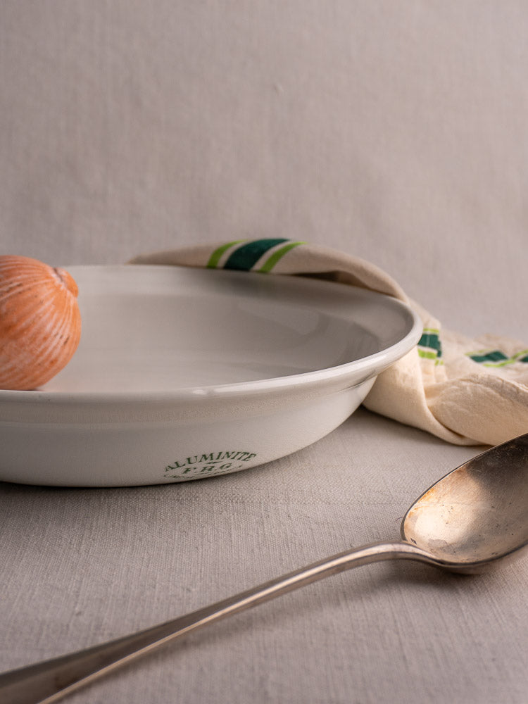 Antique French Frugier Limoges aluminite bowl with seashell, next to silver spoon and green-striped cloth.