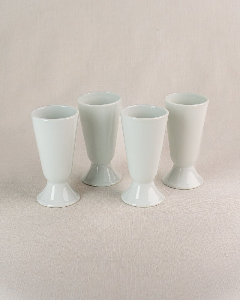 Set of four vintage French Mazagran cups in white Limoges porcelain on neutral fabric background.