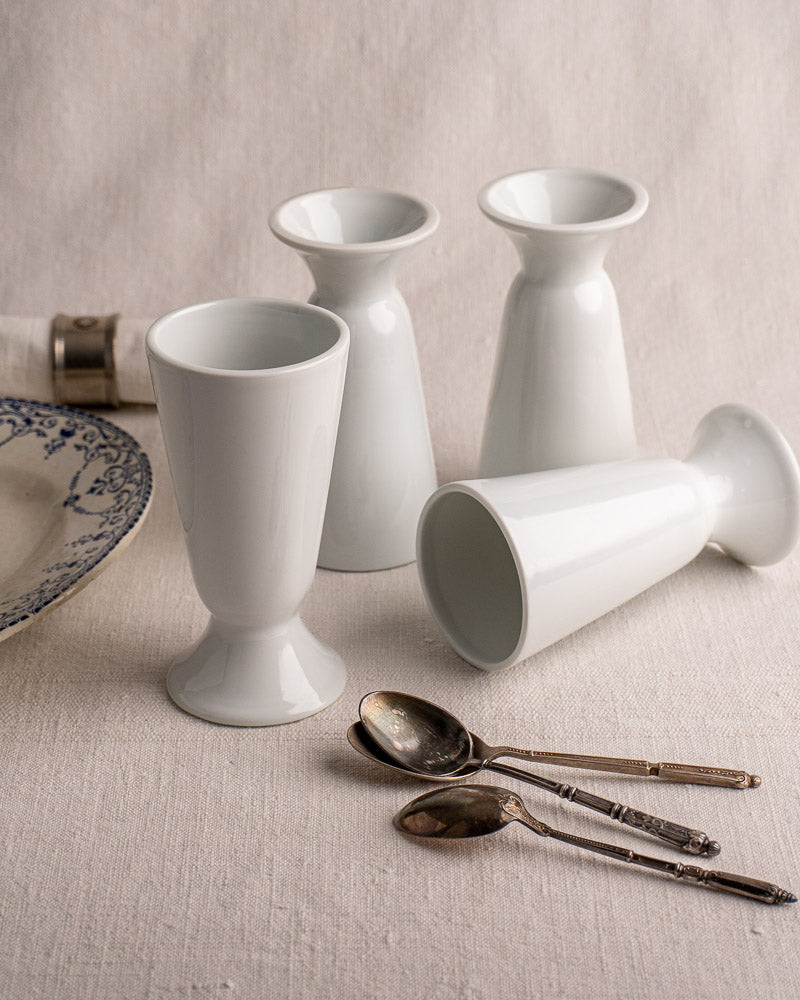 Set of four vintage French Mazagran cups in white Limoges porcelain on neutral fabric background.