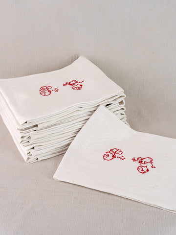 Set of twelve antique French damask linen napkins, red "P.G." monogram, on neutral surface.