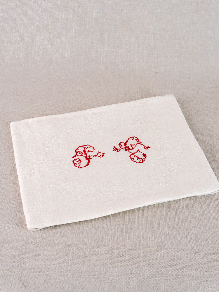 Antique French white damask linen napkin with red embroidered "P.G." monogram on neutral background.