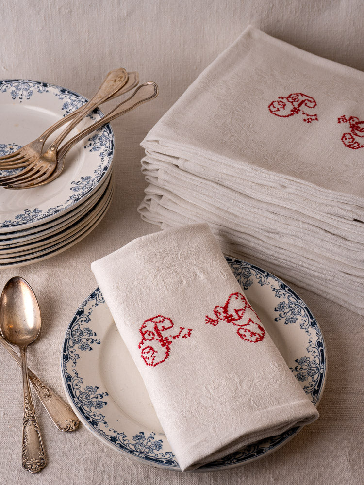 Antique French monogrammed damask linen napkins with red P.G. initials, stacked white blue-floral plates, vintage silverware.