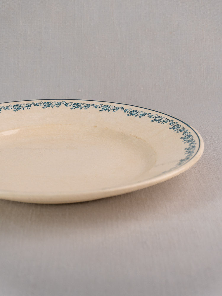 Antique French faience plate in Longwy Capucia pattern with teal floral border on light gray surface.