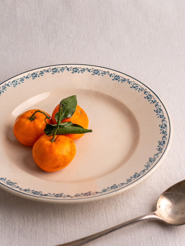 Antique French Longwy Capucia faience plate with teal floral border, tangerines, on white tablecloth with silver spoon.