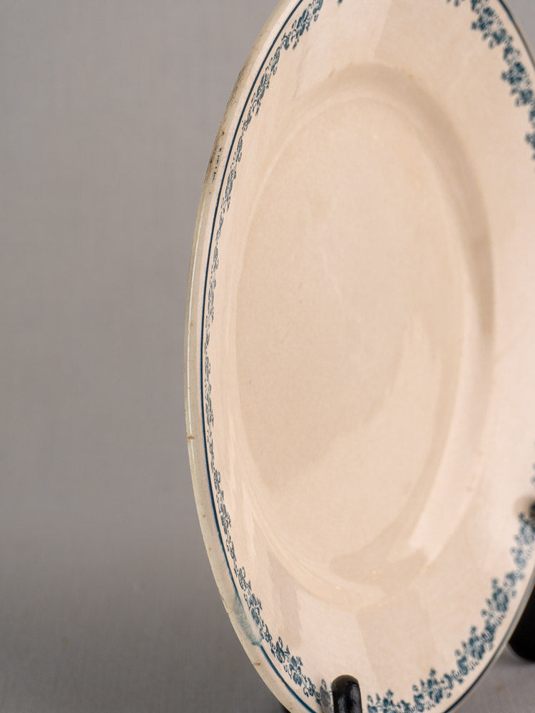 Antique French faience plate with teal Longwy Capucia floral border on black stand, gray background.