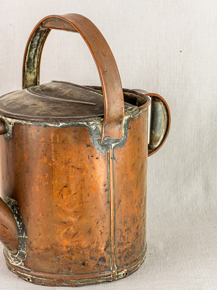 Antique French copper hand-hammered watering can with large curved handle and aged patina.