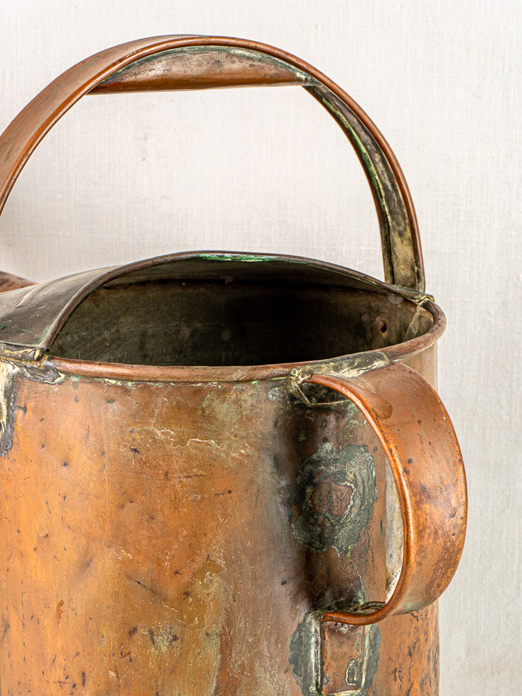 Antique French copper hand-hammered watering can with large handle and aged patina, neutral background.