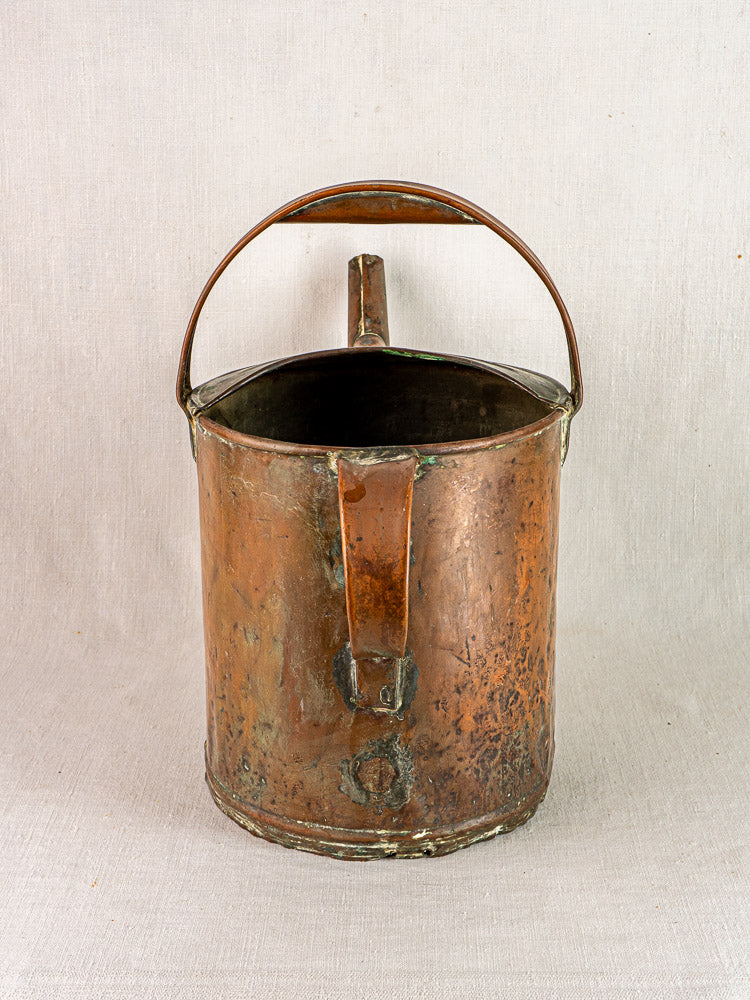 Antique French hand-hammered copper Arrosoir watering can with handle and spout on beige fabric.