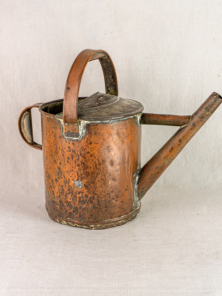 Antique French copper conservatory arrosoir with curved handle and right-side spout, set on neutral fabric.