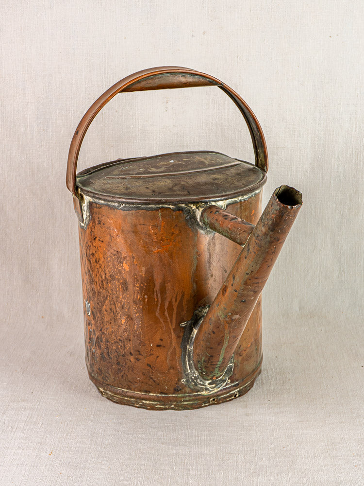 Antique French copper Arrosoir watering can with large handle and angled spout on beige fabric.