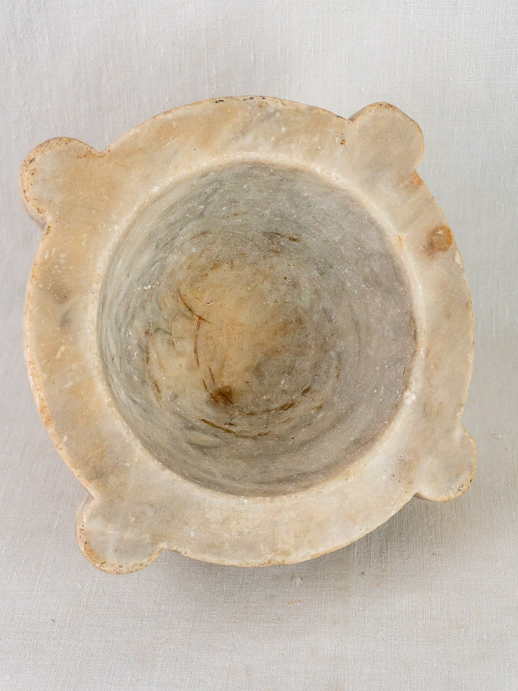 Antique French hand-carved stone mortar and pestle with four protruding corners on light fabric background.