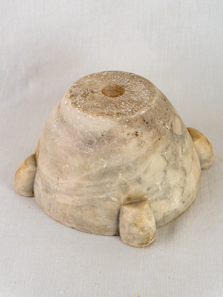 Antique French marble mortar and pestle with three rounded feet, weathered patina, on light fabric.