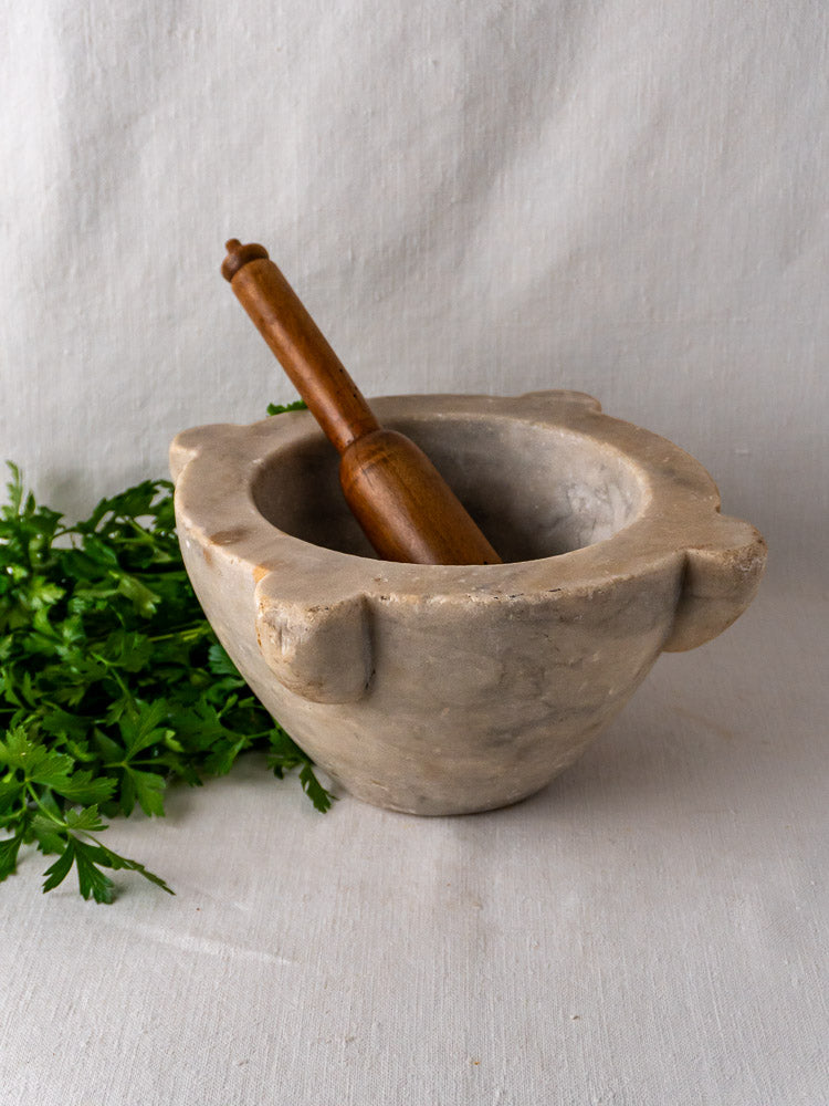 Antique French marble mortar and pestle displayed on light cloth with fresh parsley nearby.