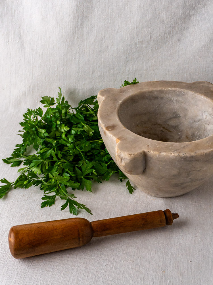 Antique French marble mortar and pestle on white cloth with fresh parsley nearby.