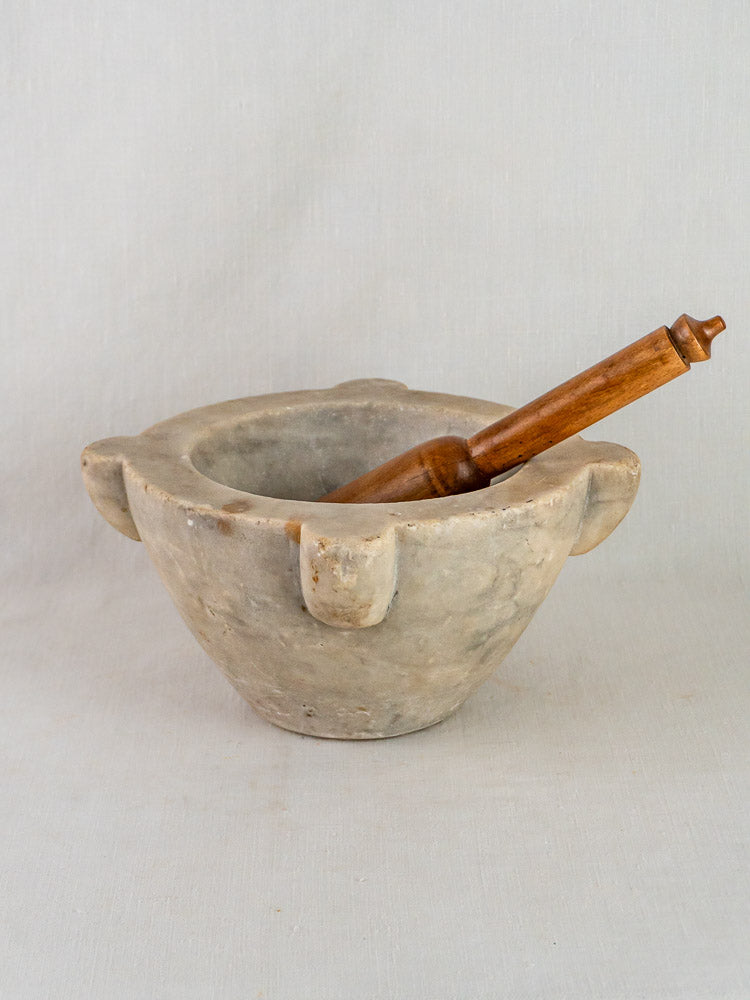 French antique marble mortar and wooden pestle with three lugs on a light background.
