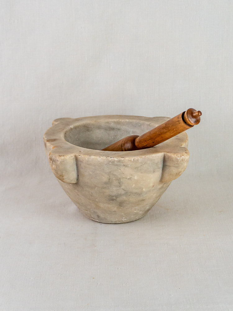 Antique French hand-carved marble mortar and pestle on a light gray surface, plain gray backdrop.