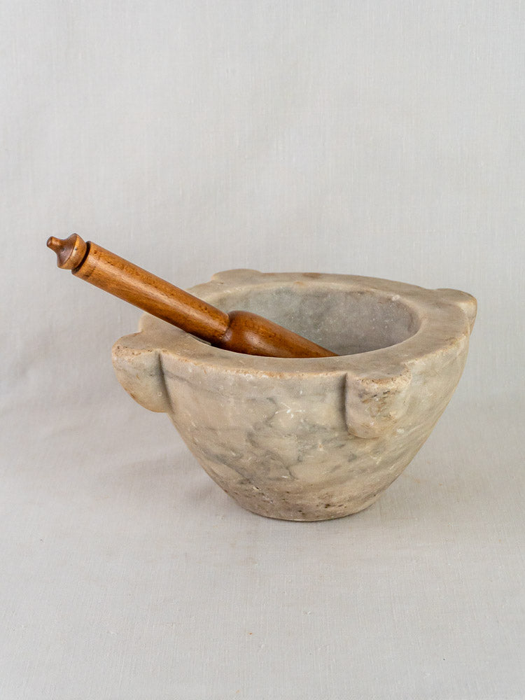 Antique French hand-carved stone mortar with wooden pestle on a neutral surface, plain background.