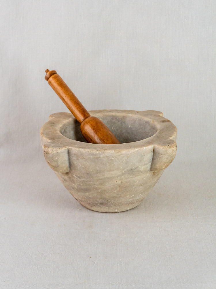 Antique French hand-carved gray stone mortar with wooden pestle on a light gray surface.