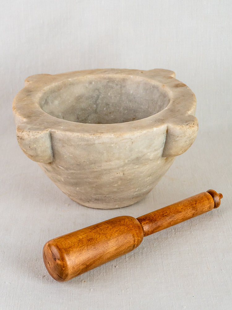 Antique French marble mortar with thick handles and wooden pestle on a light background.