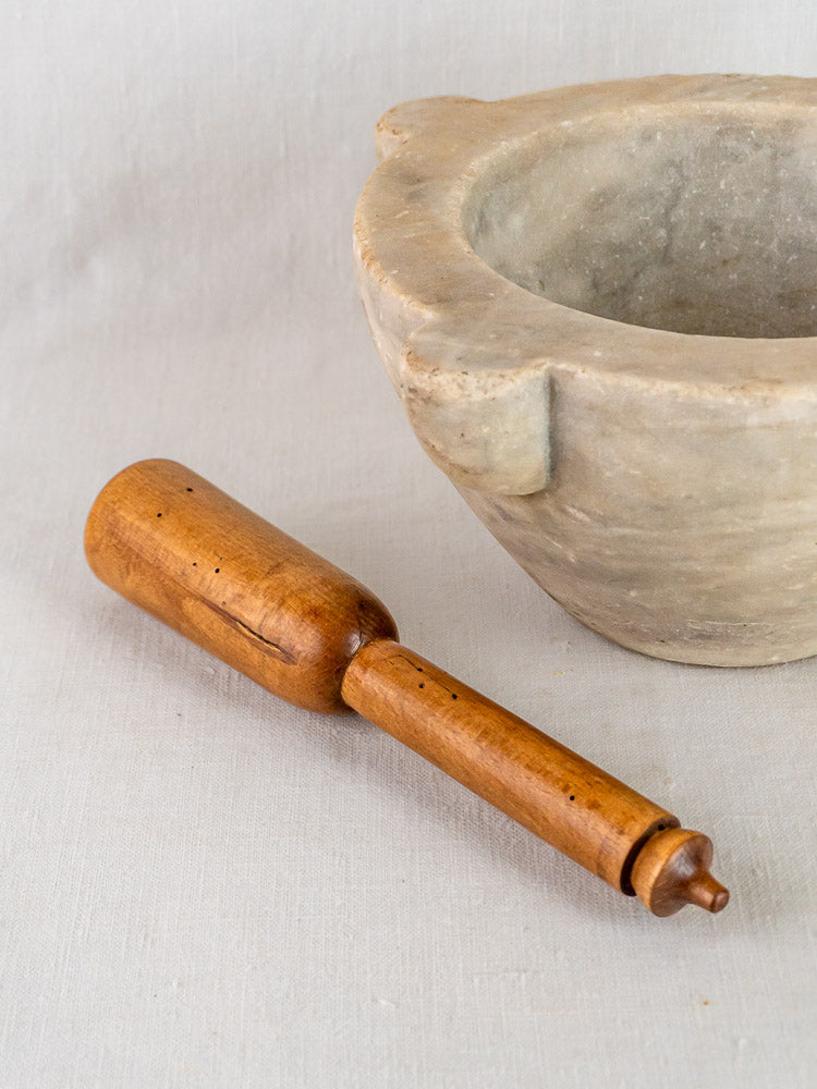 Antique French hand-carved marble mortar with wooden pestle resting on a light fabric surface.