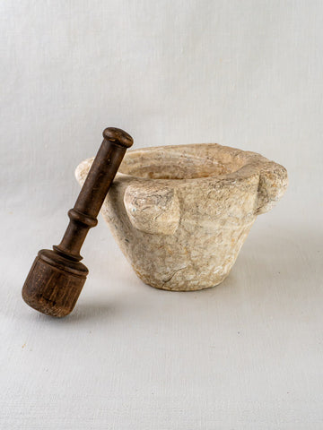Antique French marble mortar with two handles and dark wooden pestle on light cloth surface.
