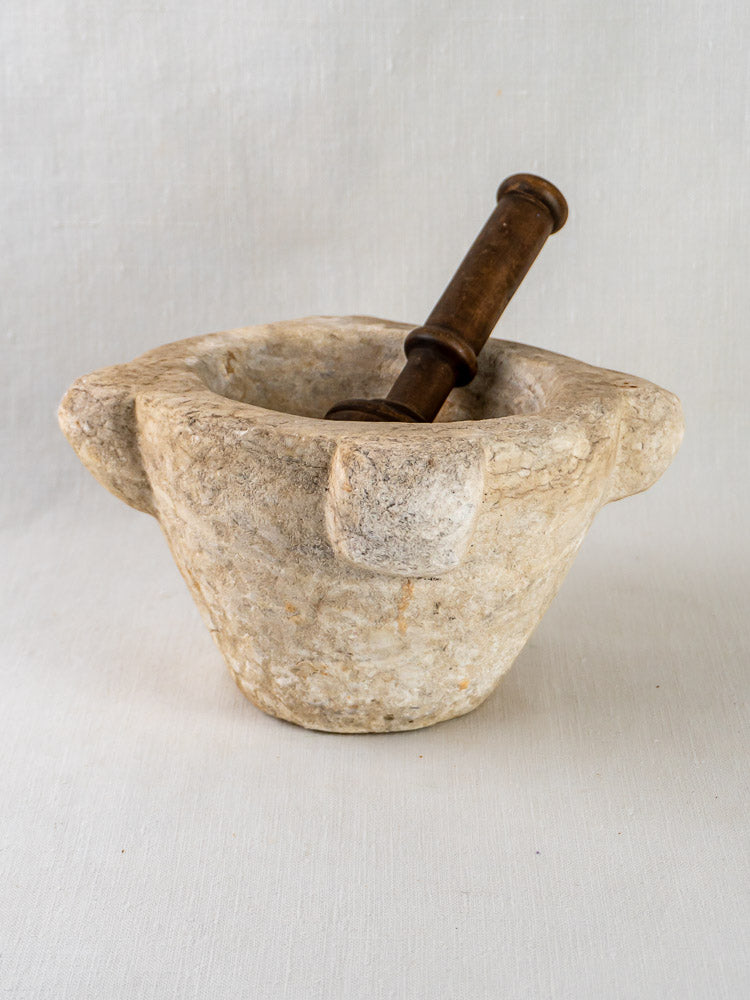 Antique French hand-carved marble mortar with wooden pestle, on a white surface against a light background.