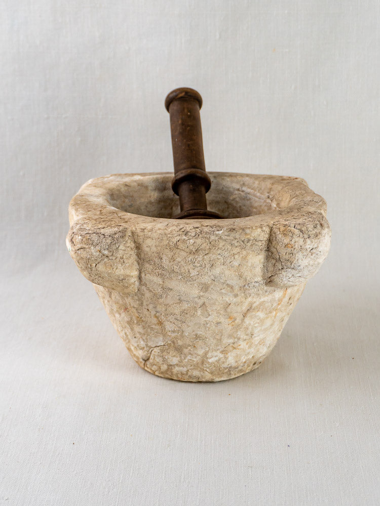 Antique French marble mortar and wooden pestle on a light fabric background.