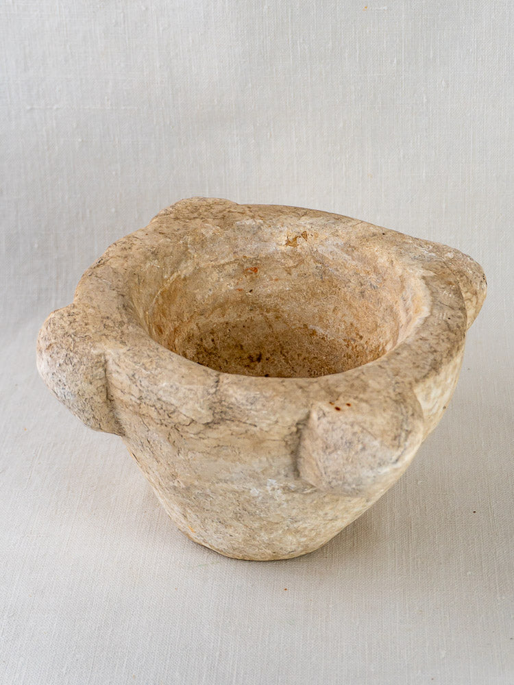 Antique French hand-carved marble mortar and pestle with two side handles on light fabric.