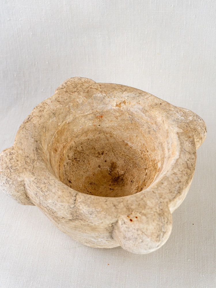 Antique French marble mortar and pestle with four rounded lobes on light fabric backdrop.