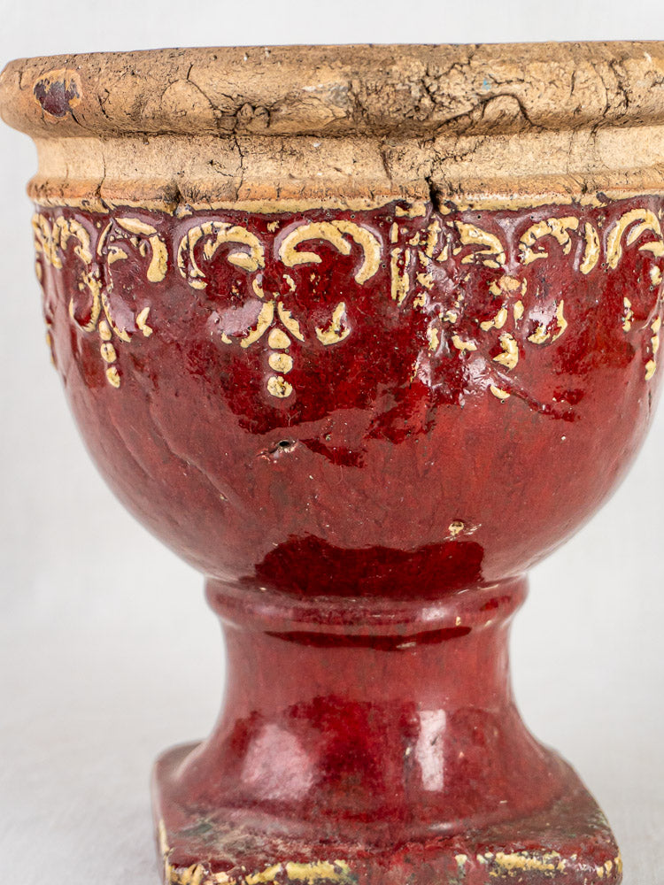 Oxblood French terracotta urn with yellow rim patterns, cracked glaze, and distressed French provincial finish.