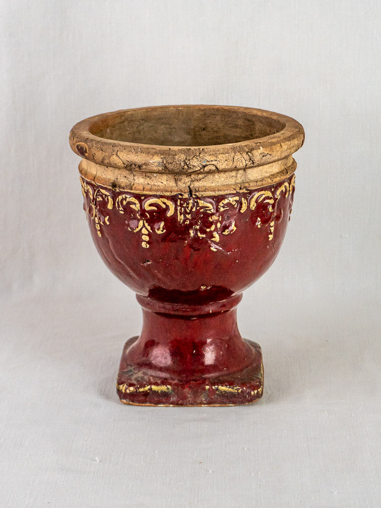 Antique French red terracotta urn with gold accents and rustic glaze on square base, light gray background.