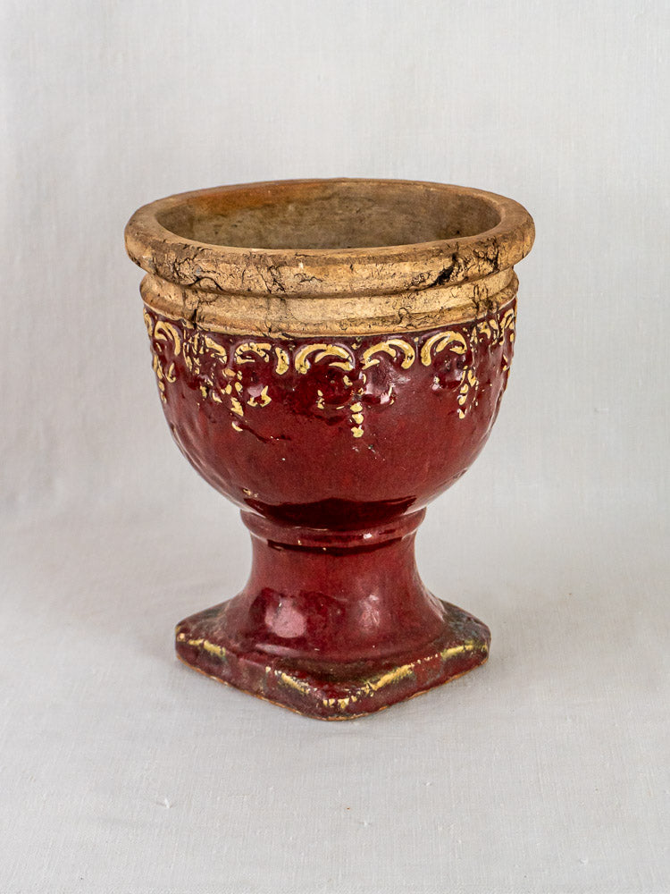 Antique-style French terracotta urn with gold accents, glossy maroon glaze, and square base on light background.
