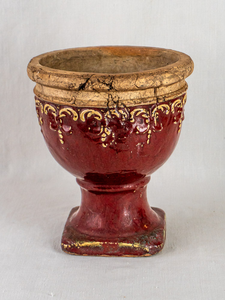 Antique French terracotta urn with red and gold glaze, detailed rim, square base, aged patina.