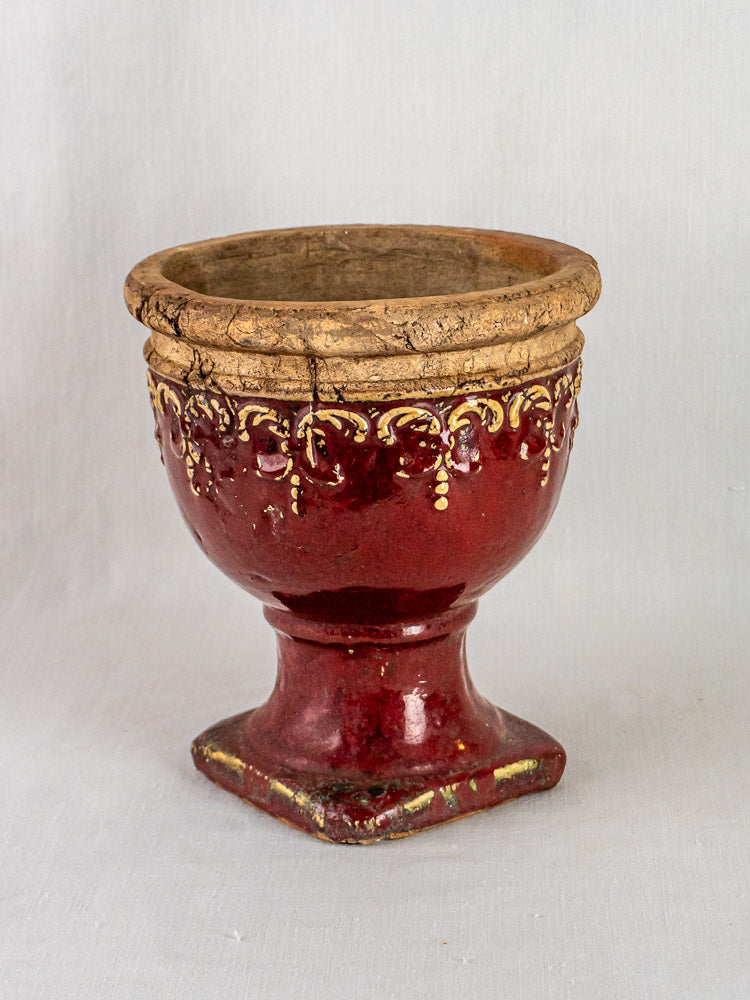 Antique French terracotta cache-pot with oxblood glaze, yellow rim accents, square base, on light background.