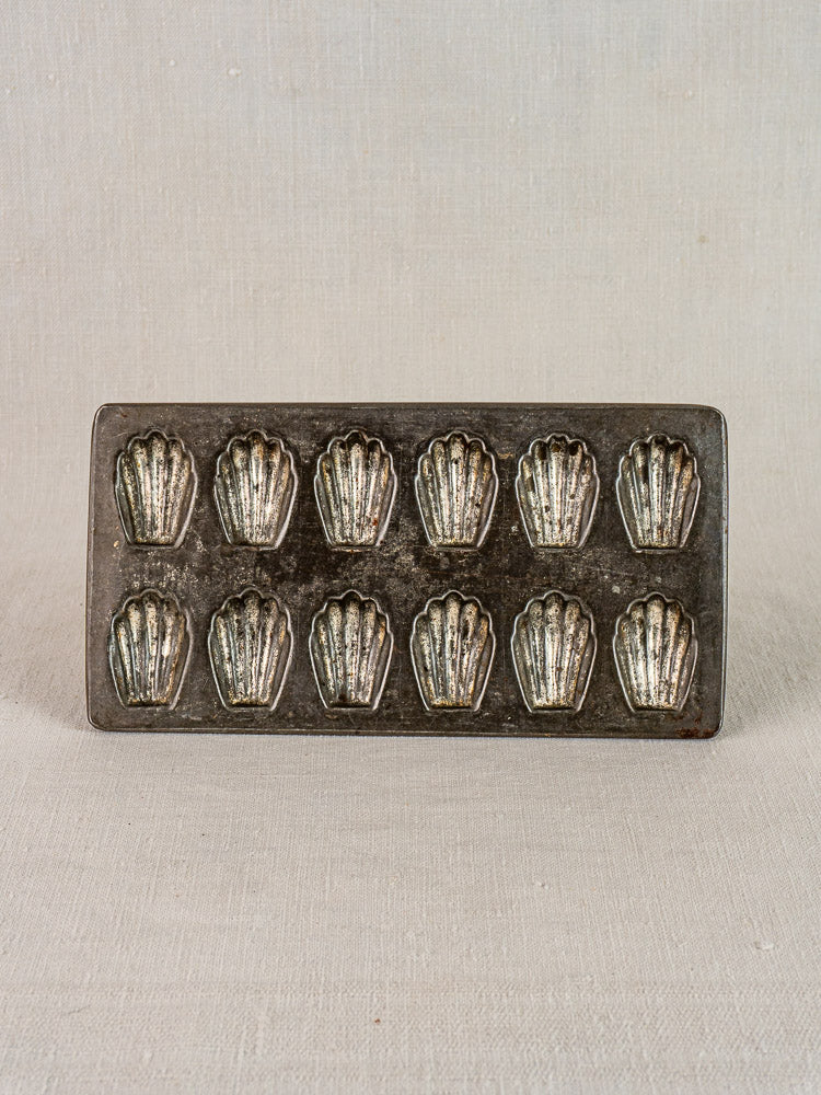 Antique French tinned steel mini madeleine pan with ten shell molds, on neutral fabric.