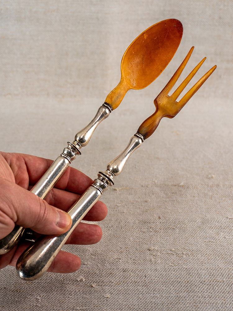 Antique French salad servers with amber horn and silver plate heads, ornate handles, on beige background.
