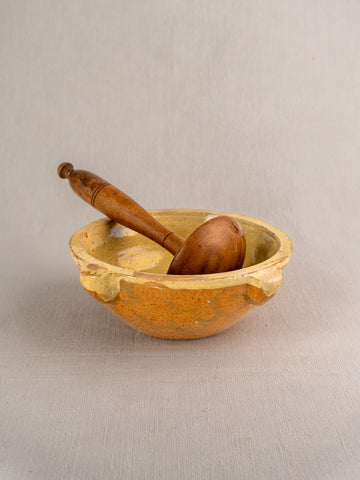 French yellow glazed mortar and wooden pestle with rustic finish on a textured beige surface.