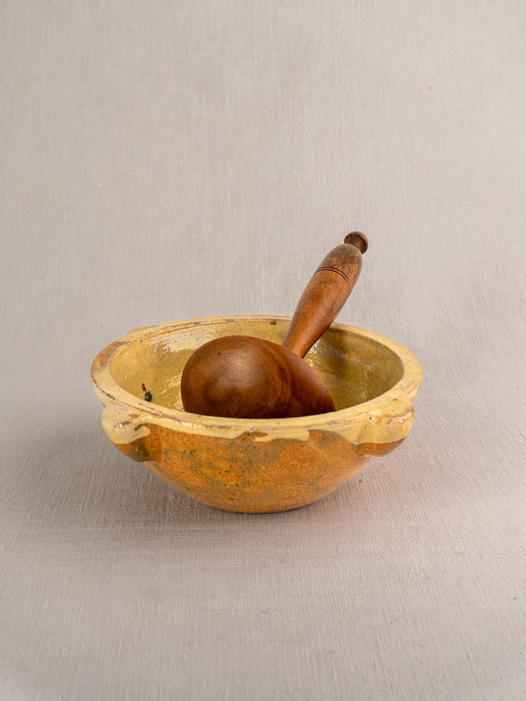 Antique French yellow glazed mortar with brown wooden pestle, displayed on a light grey surface.