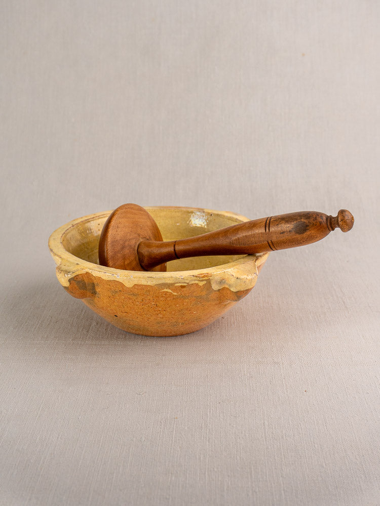 Late 19th-century French yellow glazed ceramic mortar with chipped rim and wooden pestle on fabric.