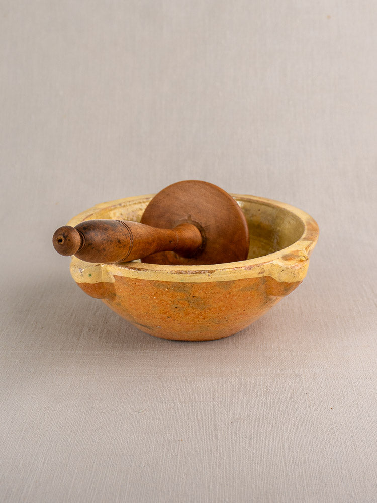 Antique French yellow glazed mortar with wooden pestle, rustic Provençal style on neutral fabric background.