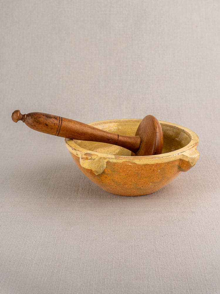 Antique French yellow glazed ceramic mortar with wooden pestle on light gray textured surface.