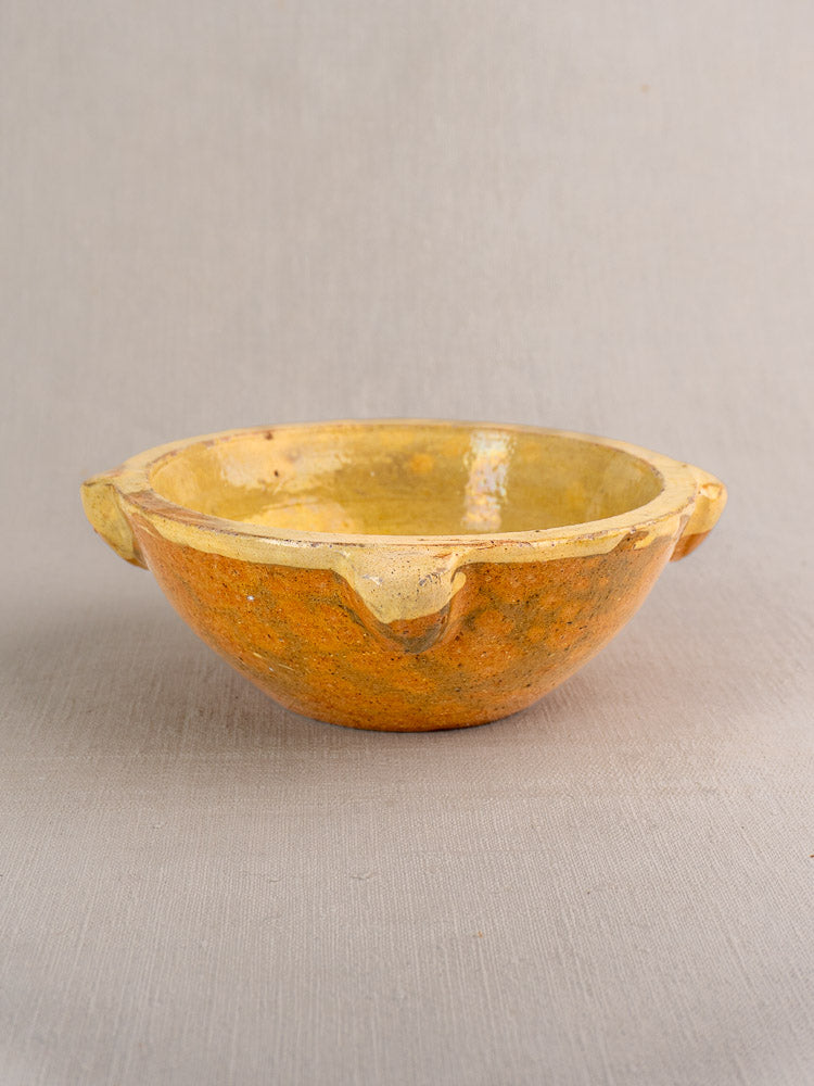 French yellow glazed ceramic mortar with rustic finish and three spouts on neutral fabric surface.