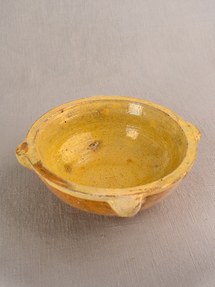 Antique French yellow glazed mortar and pestle with side handles, rustic finish, on textured surface.